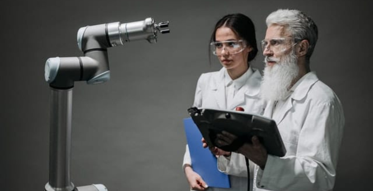 Dois cientistas usando óculos de segurança analisam um braço robótico em um laboratório, representando tecnologias da Indústria 4.0.