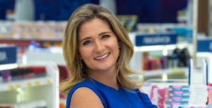 Patriciana Queirós em farmácia, símbolo de inovação no setor farmacêutico, vestindo azul e sorrindo.