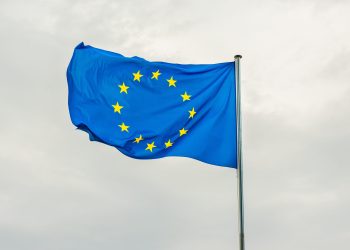 A imagem mostra a bandeira da União Europeia tremulando ao vento.