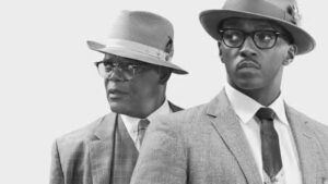 Cena do filme O Banqueiro com os personagens Joe Morris e Bernard Garrett, retratando luta contra racismo no sistema bancário dos EUA.