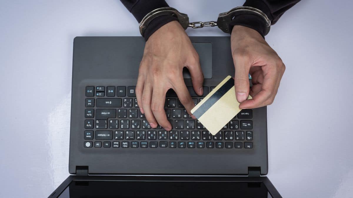 Pessoa algemada usando cartão de crédito em fraude online, destacando a importância da prevenção a fraudes no sistema financeiro.