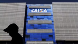 Fachada de prédio da Caixa com uma silhueta de pessoa passando pela frente do local. Caixa Seguridade bateu recorde em 3T24.