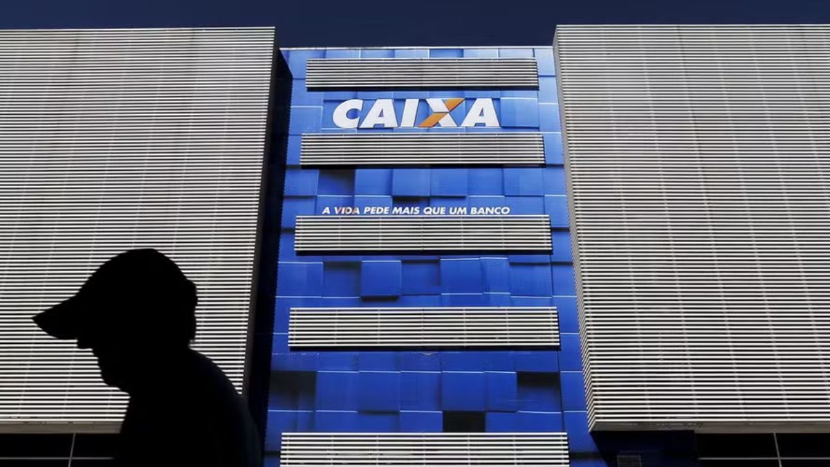 Fachada de prédio da Caixa com uma silhueta de pessoa passando pela frente do local. Caixa Seguridade bateu recorde em 3T24.