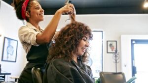 Mulher cortando cabelo em salão de beleza; mercado da área deve crescer até 2027.