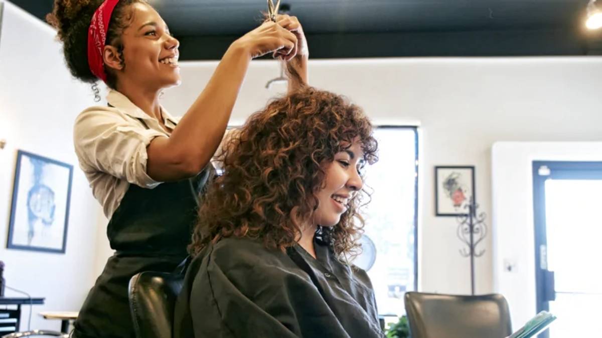 Mulher cortando cabelo em salão de beleza; mercado da área deve crescer até 2027.