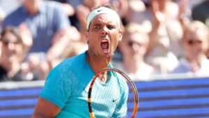 Rafael Nadal gritando em comemoração, segurando sua raquete durante um jogo, vestindo camiseta azul e faixa na cabeça, com torcida ao fundo.