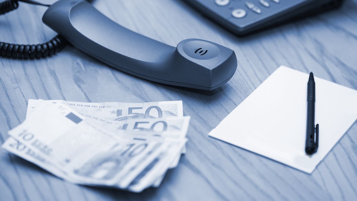 Telefone fixo em uma mesa, ao lado de notas de dinheiro.
