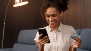 Mulher sorrindo enquanto usa o celular para negociação de dívidas.