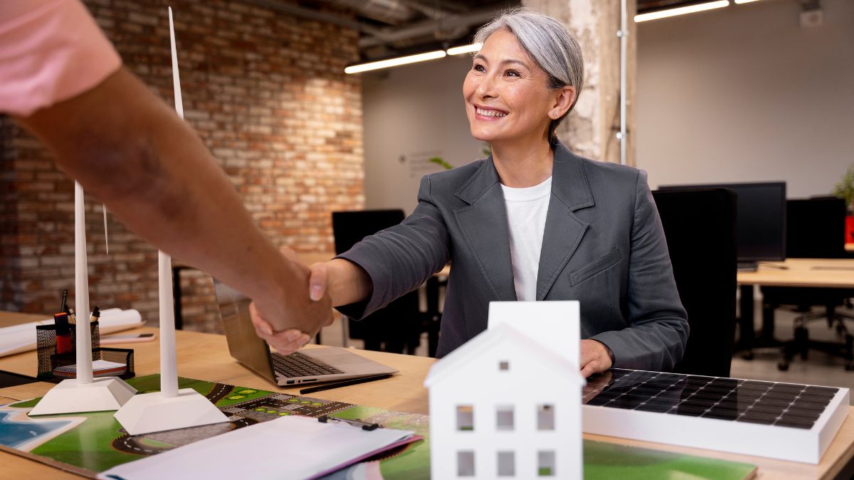 Corretora imobiliária sorrindo e apertando a mão de um cliente.