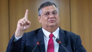 Imagem com Flávio Dino, ministro do STF, erguendo o dedo indicador da mão direita. Após questionamentos, Dino concede liberação parcial de emendas bloqueadas