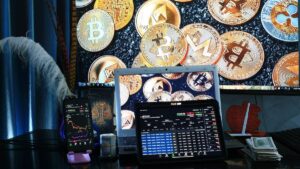 Na imgem, um computador com moviemnto de ações em volta de criptomoedas douradas. Isso em meio à lista do BTG Pactual sobre as melhores opções de investimentos para 2025