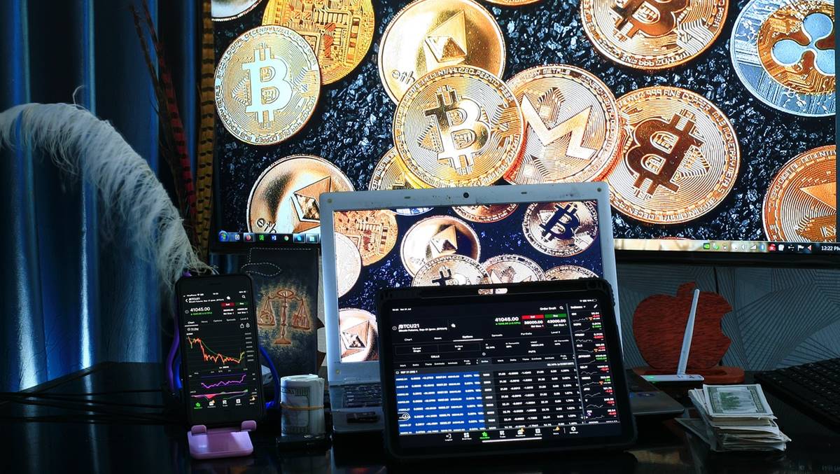 Na imgem, um computador com moviemnto de ações em volta de criptomoedas douradas. Isso em meio à lista do BTG Pactual sobre as melhores opções de investimentos para 2025