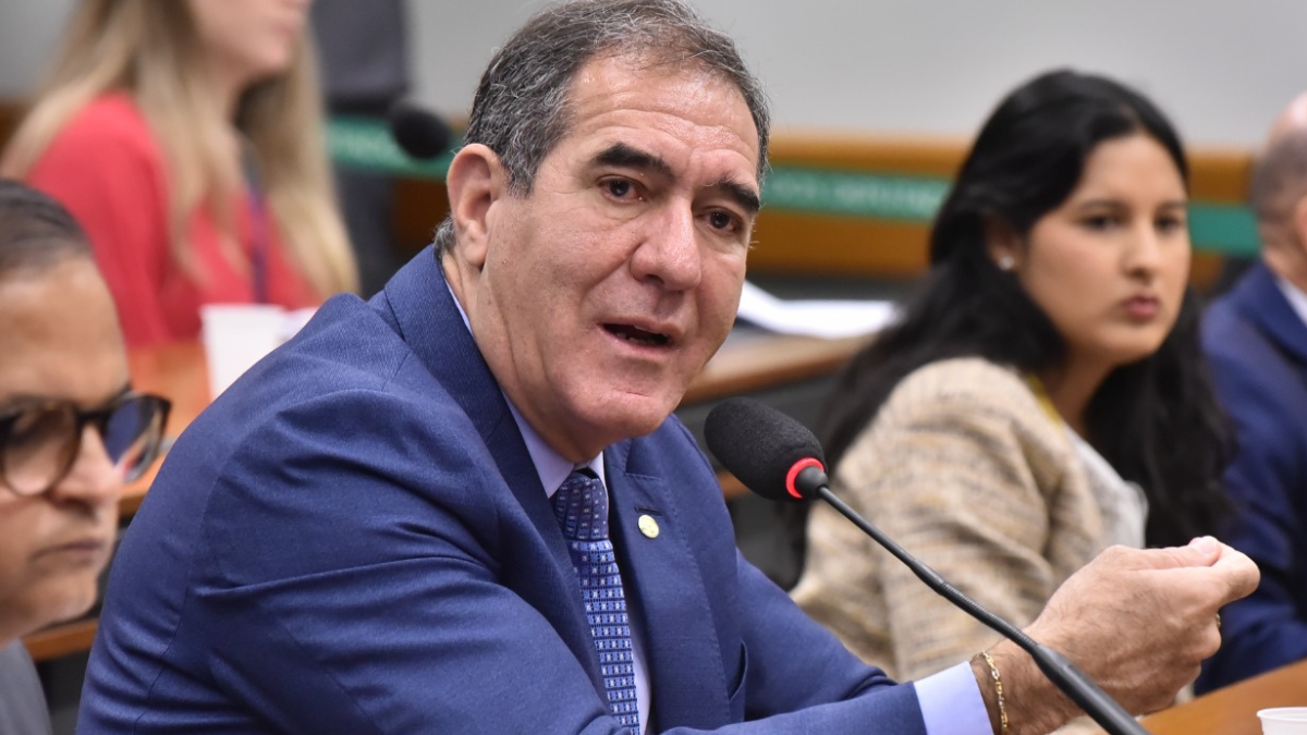 Luiz Gastão, deputado federal, discute sobre o adicional da CSLL para multinacionais durante sessão parlamentar, com outros participantes ao fundo.