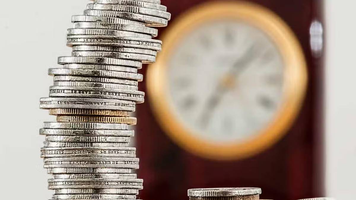 Imagem com moedas de prata uma sobre as outras e relógio ao fundo. Fim da taxa de custódia a partir de janeiro de 2025