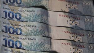 Na imagem notas de 100reais em meio ao relatório que mede os desafios do déficit zero em 2025