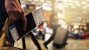 Imagem de um homem no aeroporto segurando um passaporte e uma passagem aérea para ilustrar uma matéria jornalística sobre o passaporte do Brasil.