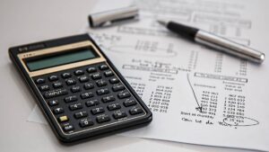 Na imagem consta uma calculadora, uma caneta e uma fatura com valores. Regulamentação do CMN aprova uso de imóvel para mais de um financiamento
