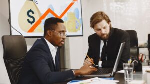 Dois homens conversando e apontando para um computador, representando empresários que querem investir no Brasil.