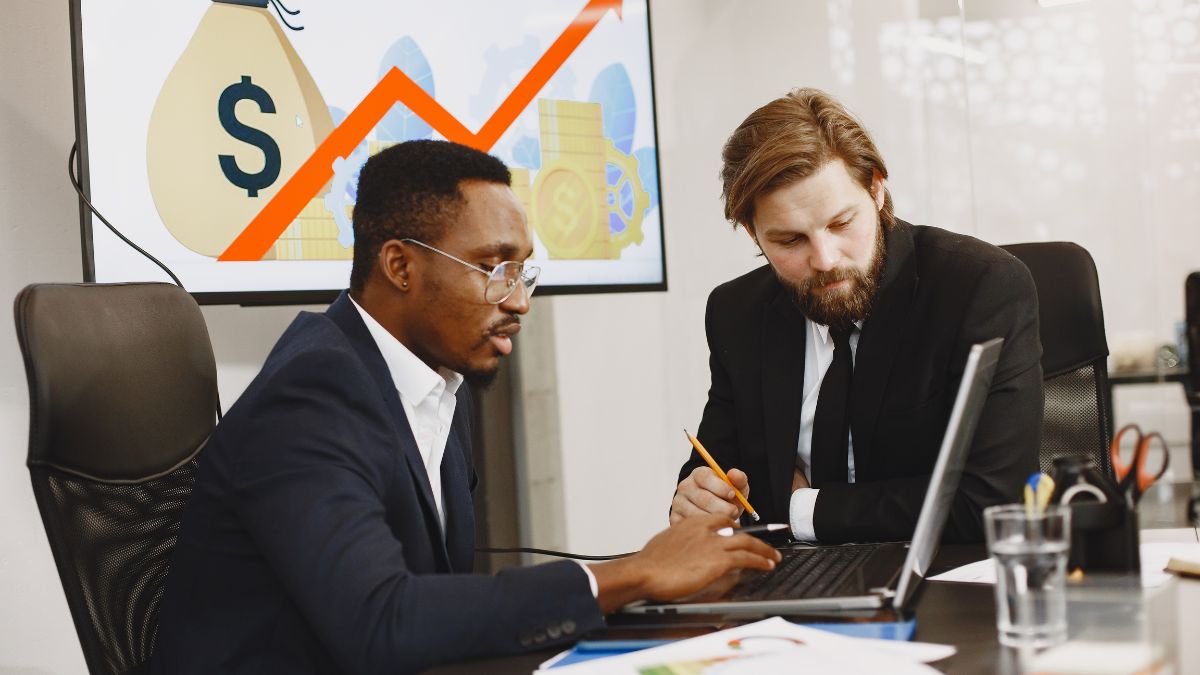 Dois homens conversando e apontando para um computador, representando empresários que querem investir no Brasil.