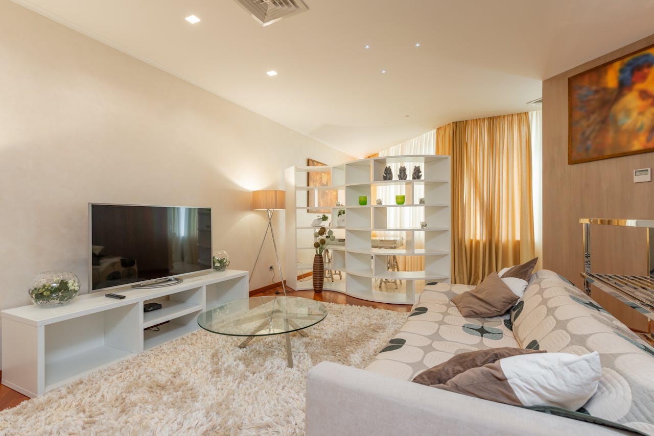 Sala de estar moderna com sofá, TV, mesa de centro de vidro e estante decorativa, representando um apartamento para locação flexível.