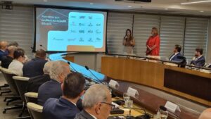 BScash fecha parceria nacional na 14ª Reunião de Diretoria da Fenavist, em Brasília. Duas palestrantes apresentam a fintech para um grupo de empresários e representantes do setor de segurança privada. No telão, são exibidos os logotipos de empresas parceiras da BScash.