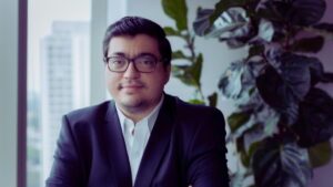 Felipe Salto, economista-chefe da Warren Investimentos, em um escritório com fundo de plantas e janelas mostrando prédios urbanos.