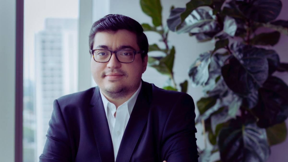 Felipe Salto, economista-chefe da Warren Investimentos, em um escritório com fundo de plantas e janelas mostrando prédios urbanos.