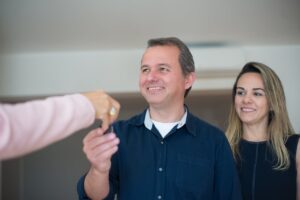 Homem sorrindo enquanto recebe as chaves de um imóvel, com uma mulher ao fundo, simbolizando locação flexível e acessibilidade no mercado imobiliário.