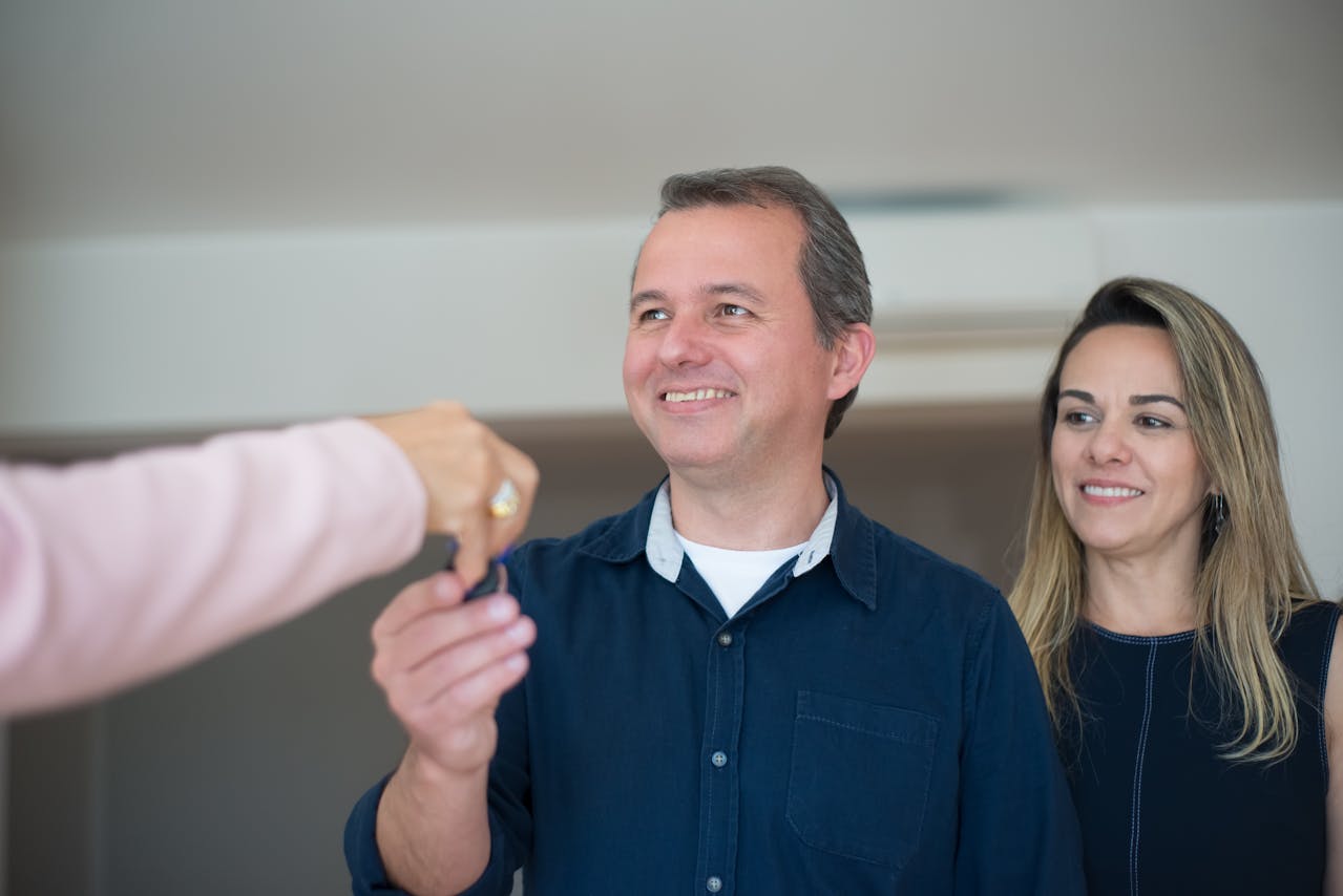 Homem sorrindo enquanto recebe as chaves de um imóvel, com uma mulher ao fundo, simbolizando locação flexível e acessibilidade no mercado imobiliário.