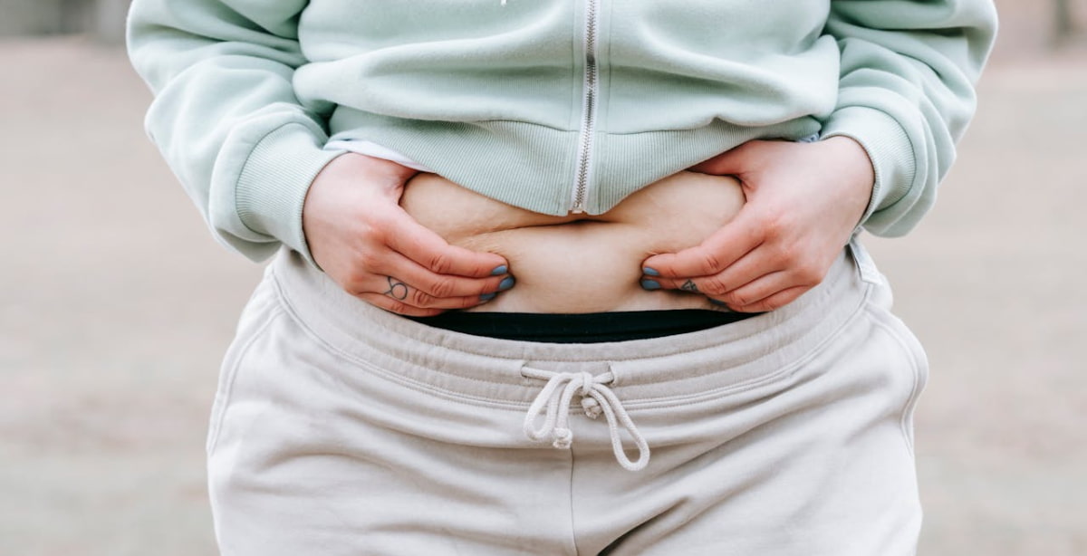 Pessoa segurando a região abdominal, ilustrando o contexto de perda de peso e tratamentos para obesidade, como os medicamentos similares ao Ozempic, que impulsionam o faturamento da EMS.