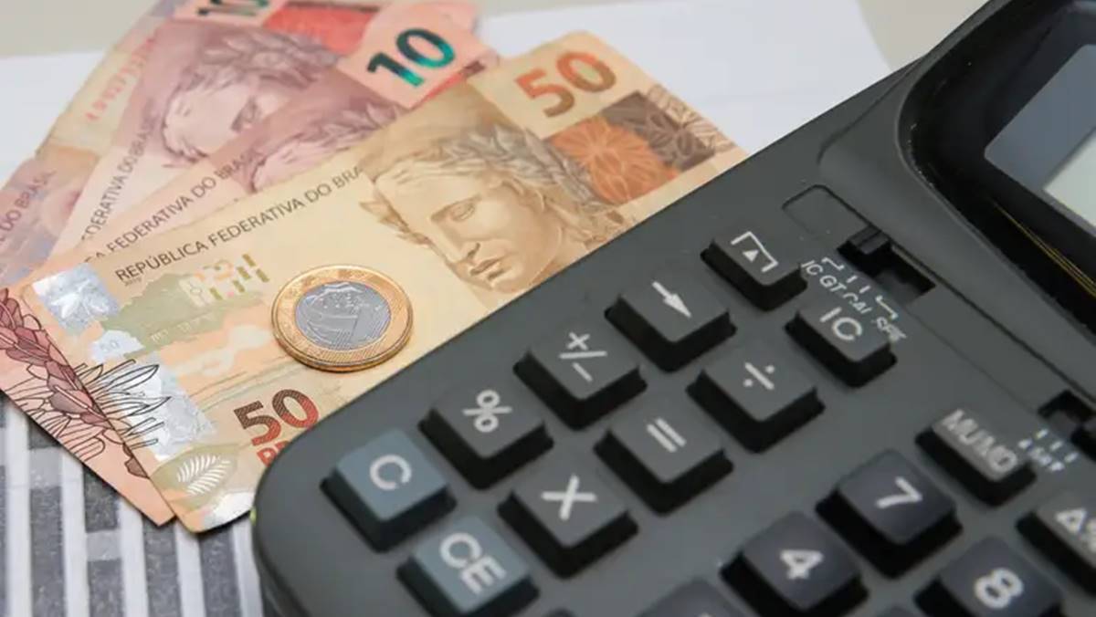Imagem de cédulas de real brasileiro ao lado de calculadora. Queda do déficit público em novembro de 2024