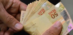 Mãos contam dinheiro em referência a economizar no IPVA