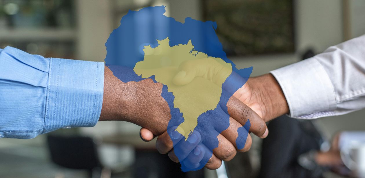 Aperto de mãos entre empresários, com sobreposição dos mapas do Brasil e da África, simbolizando o fortalecimento das relações Brasil e África.