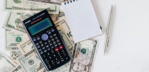 Calculadora sobre notas de dólar, bloco de anotações e caneta, representando análise financeira e impacto econômico das tarifas de Trump na América Latina.