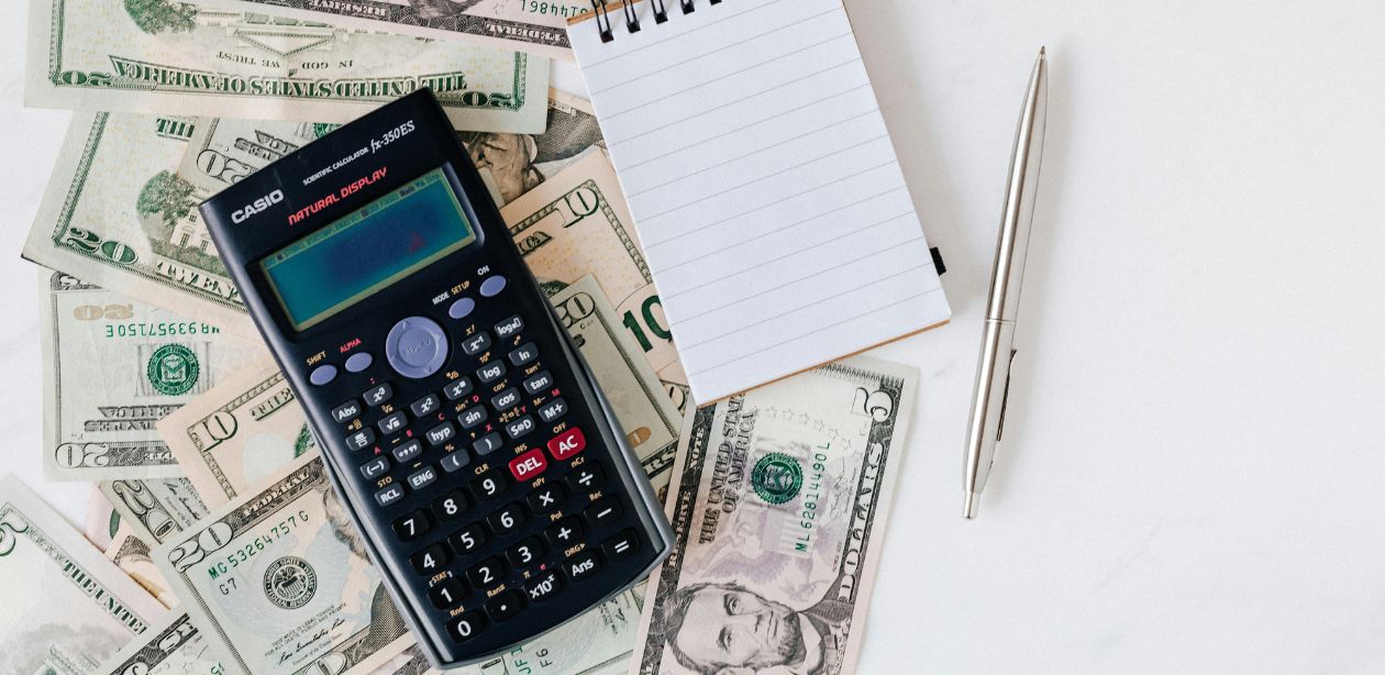 Calculadora sobre notas de dólar, bloco de anotações e caneta, representando análise financeira e impacto econômico das tarifas de Trump na América Latina.