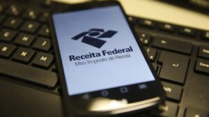 Celular em cima de um teclado de computador, com a imagem da logo da Receita Federal, representando os dados que a Receita Federal pode ver.