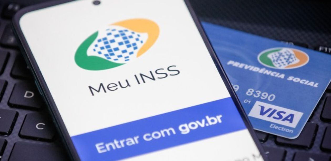 A imagem mostra um celular com a tela acesa, aparecendo o início do Portal Gov. para representar o pagamento de 13º do INSS.