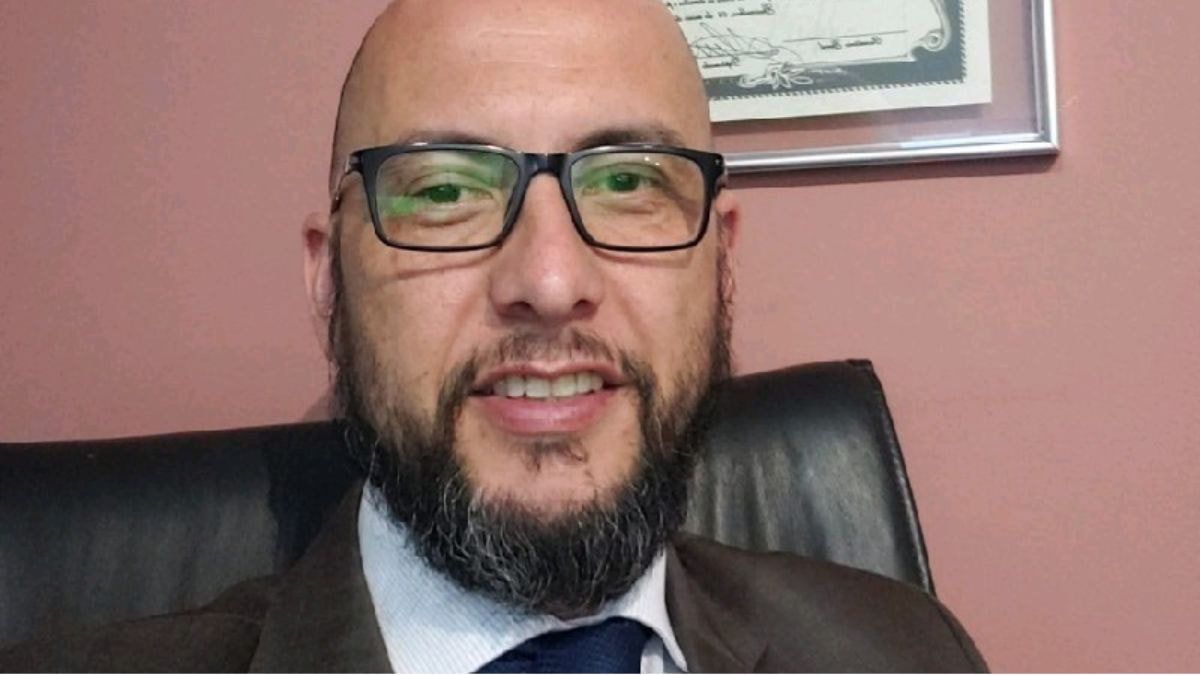 Homem de terno e gravata sorrindo em um escritório, representando os impactos das medidas comerciais de Trump no cenário global.