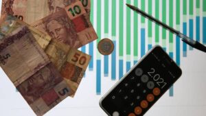 Imagem de notas de reais, moeda e calculadora. Alta da dívida pública