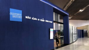 Entrada da Sala VIP da American Express no Aeroporto de Guarulhos, com fachada azul e o slogan 'Não viva a vida sem o seu'.