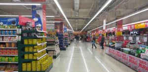 A imagem mostra o corredor de um supermercado ou loja de bairro, com várias prateleiras e vários produtos diversificados.