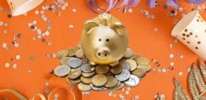 A imagem mostra um fundo laranja cheio de confetes, representando o Carnaval 2025. No centro um cofre em formato de porco dourado em cima de muitas moedas.