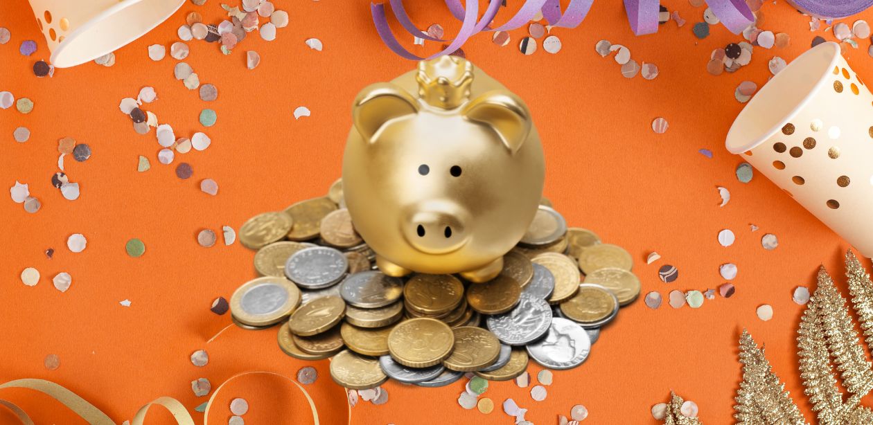 A imagem mostra um fundo laranja cheio de confetes, representando o Carnaval 2025. No centro um cofre em formato de porco dourado em cima de muitas moedas.