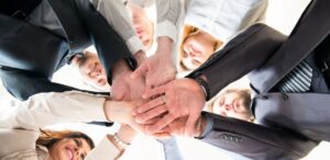A imagem mostra um grupo de pessoas em círculos com as mãos umas sobre as outras, simbolizando as as cooperativas digitais.