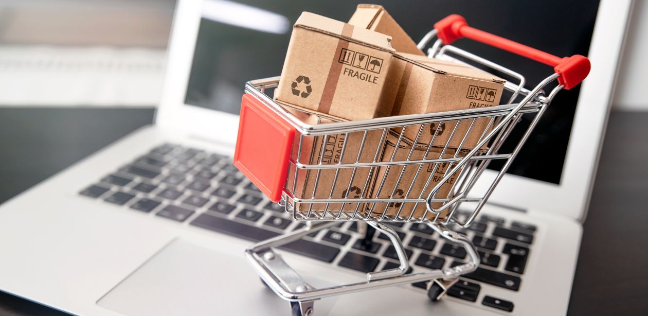 A descrição mostra um carrinho de supermercado cheio de caixas de compras em cima de um notebook, representando o crescimento do e-commerce no Brasil.
