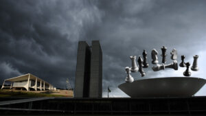 Imagem do Palácio do Planalto e do Congresso Nacional sob um céu nublado, representando a crise política no Brasil. No topo da cúpula do Congresso, peças de xadrez flutuam no ar, simbolizando a instabilidade e o jogo de poder entre Executivo, Legislativo e Judiciário.