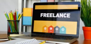 A imagem mostra um notebook está sob uma mesa, com a tela acesa escrito "Freelancer", represenrando a Economia Gig.