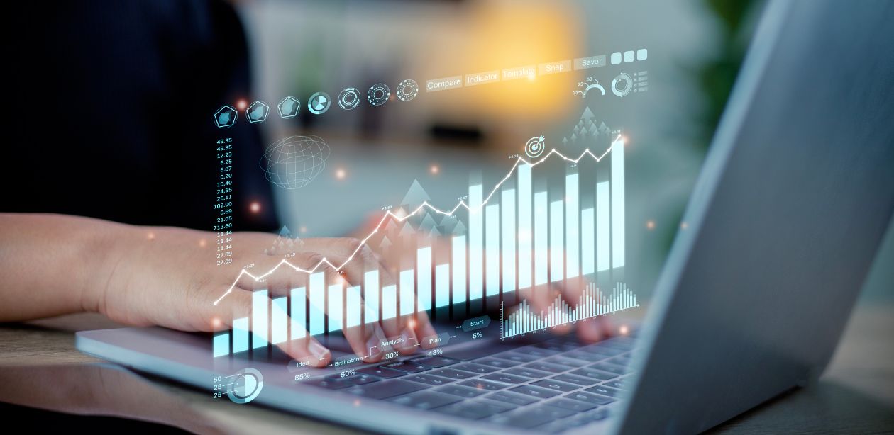 A imagem mostra uma pessoa digitando em um notebook e em cima do teclado, ícones tecnológicos, representando como a inteligência artificial nos negócios está redefinindo o mercado.