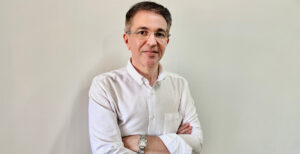 Jackson Pereira Jr., CEO do Economic News Brasil, posando com os braços cruzados e vestindo camisa branca. Imagem representa a liderança e o crescimento do portal nas redes sociais."