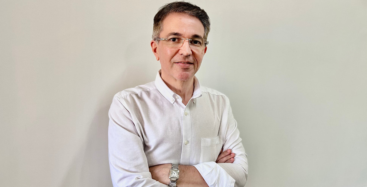 Jackson Pereira Jr., CEO do Economic News Brasil, posando com os braços cruzados e vestindo camisa branca. Imagem representa a liderança e o crescimento do portal nas redes sociais."